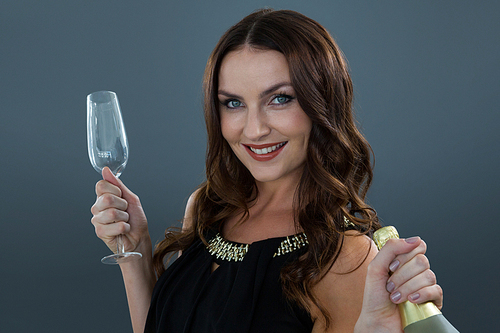Portrait of smiling woman holding champagne bottle and glass against grey background