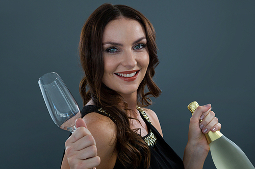 Portrait of smiling woman holding champagne bottle and glass against grey background