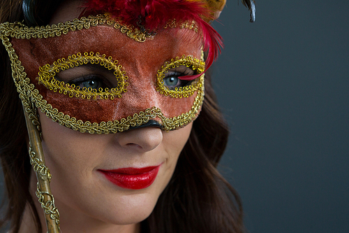 Close-up of beautiful woman wearing masquerade mask against grey background