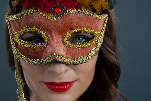 Portrait of beautiful woman wearing masquerade mask against black background