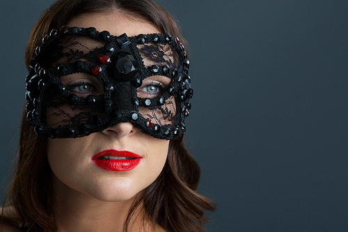 Beautiful woman wearing masquerade mask against black background