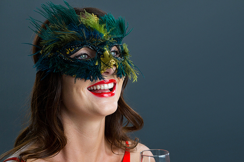 Smiling woman wearing masquerade mask against black background