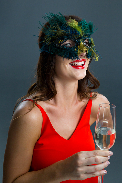 Smiling woman wearing masquerade mask and having glass of champagne