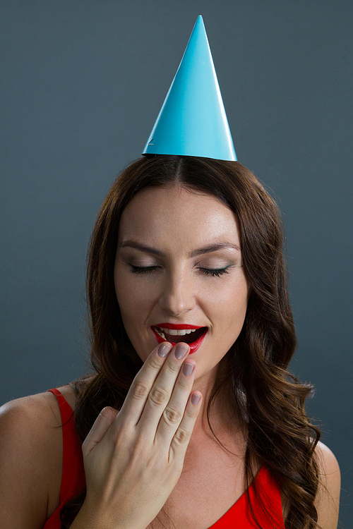 Beautiful woman in party hat yawning against black background