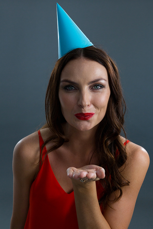 Smiling woman wearing party hat and giving flying kiss against black background