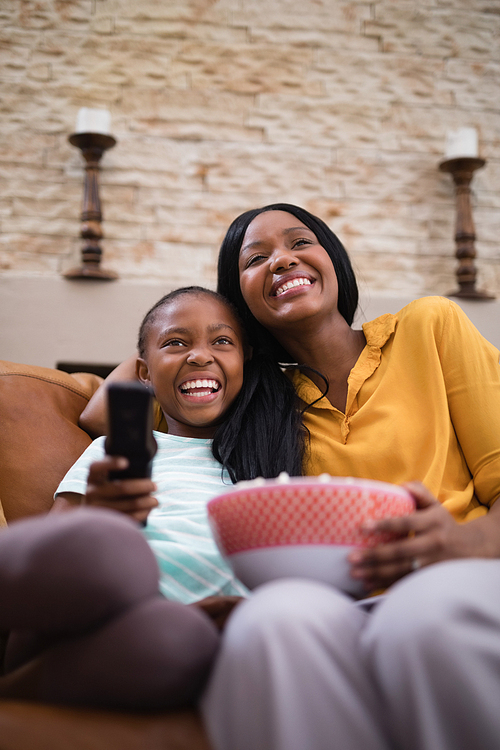 Low angle view of cheerful mother and daughter enjoying television at home