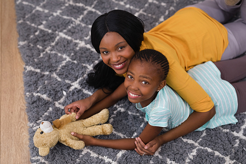 High angle view of mother and daughter with teddy bear while lying on rug at home