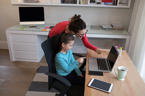 Mother assisting daughter in using laptop at desk