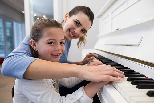 Portrait of mother assisting daughter in playing piano at home