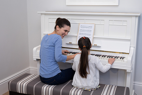 Portrait of mother assisting daughter in playing piano at home