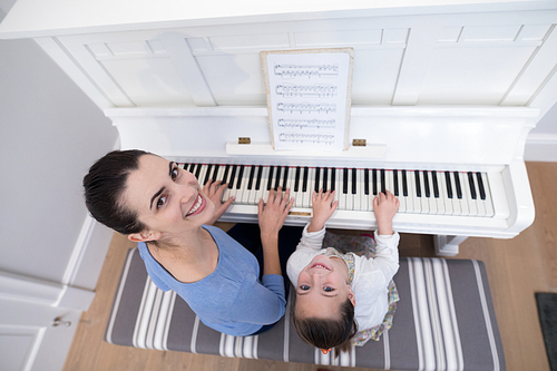 Overhead of mother assisting daughter in playing piano at home