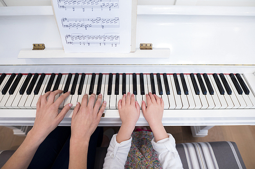 Mid section of mother and daughter playing piano at home