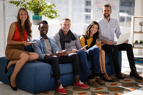 Business colleagues using electronic devices while sitting on sofa in the office