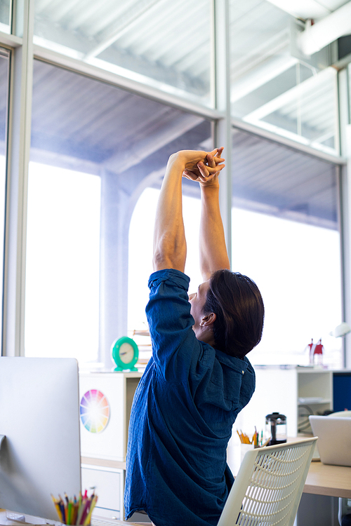 Male executive stretching hands at his desk in office