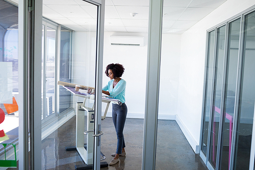 Female architect working on blueprint over drafting table in office