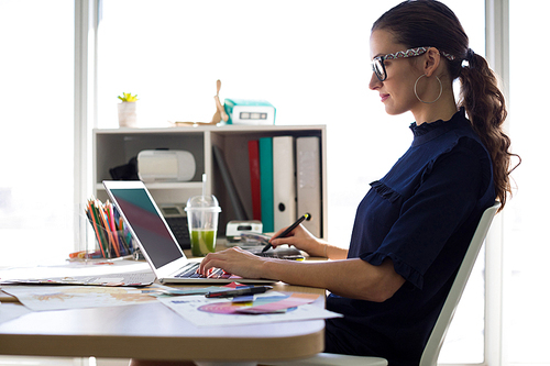 Female executive working over laptop and graphic tablet at her desk in office