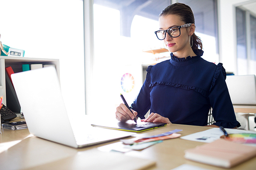 Female executive working over laptop and graphic tablet at her desk in office