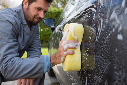 Male auto service staff washing a car roof with sponge