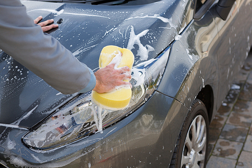 Male auto service staff washing a car bonnet with sponge