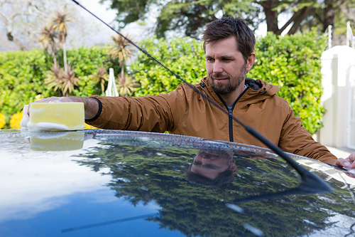 Male auto service staff washing a car roof with sponge