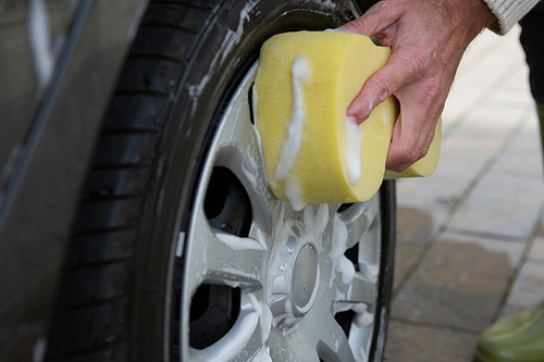 Male auto service staff washing a car tyre with sponge