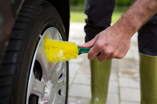 Male auto service staff washing a tyre with brush