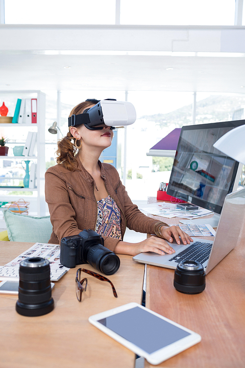 Female executive working on laptop while using virtual reality headset in office