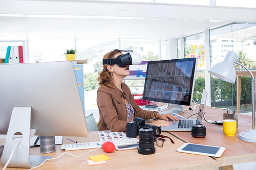 Female executive working on laptop while using virtual reality headset in office
