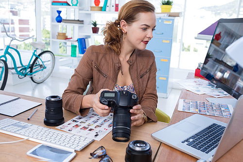 Female executive holding digital camera while looking at laptop in office