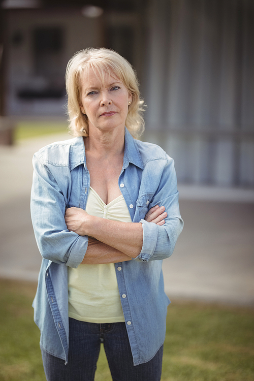 Portrait of senior woman standing with arms crossed outside her house