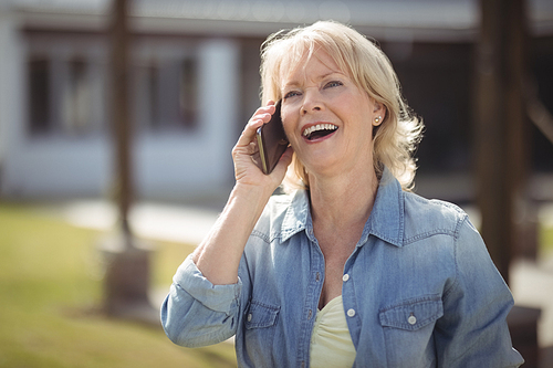 Smiling senior woman talking on mobile phone outside his house on a sunny day