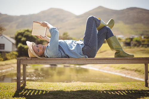 Portrait of smiling senior woman reading a book while lying on the bench in the park