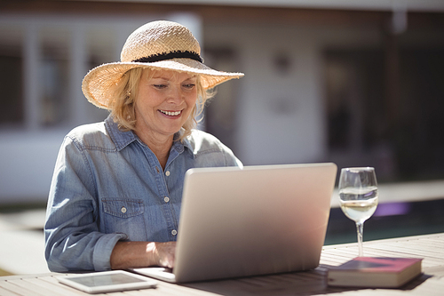 Smiling senior woman using her laptop outside house on a sunny day