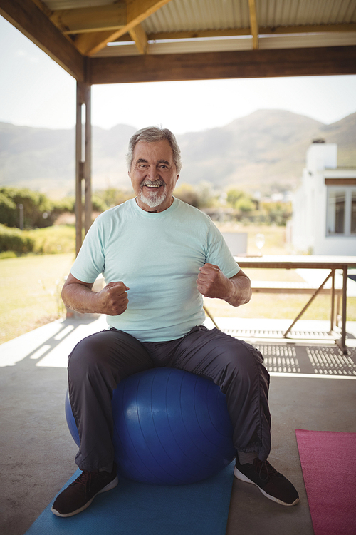 Portrait of smiling senior man sitting on fitness ball at veranda