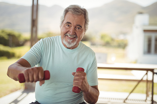 Portrait of smiling senior man exercising with dumbbells