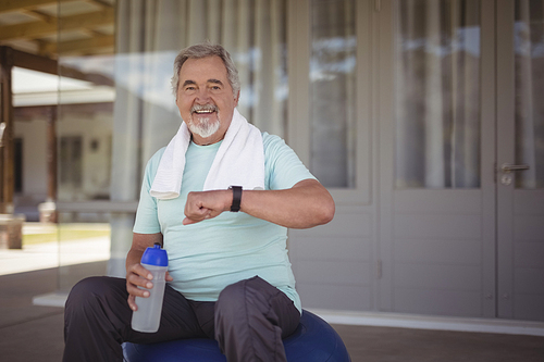 Smiling senior man checking time on wristwatch after work out at veranda