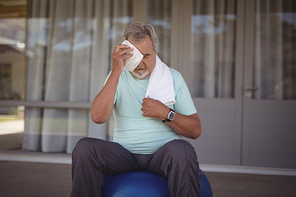 Senior man wiping sweat off his face with towel after exercising