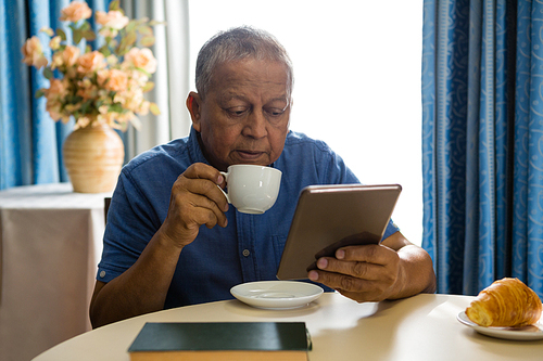 Senior man using digital tablet while having drink in nursing home