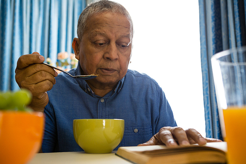 Senior man having food while reading book at table in nursing home