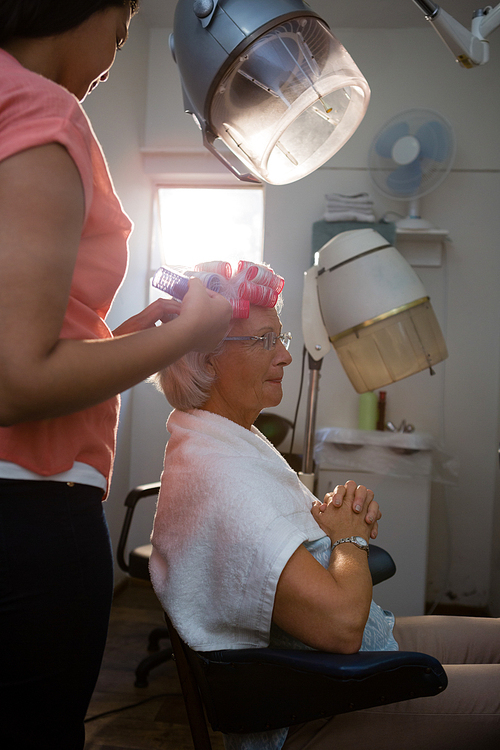 Beautician removing curlers from senior woman hair at salon