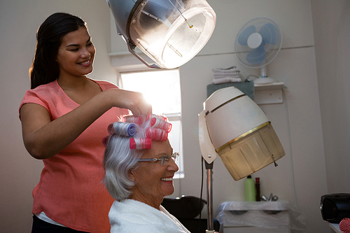 Smiling beautician removing curlers from senior woman hair at salon