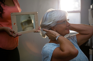 Midsection of hairstylist showing hair in mirror to senior woman at salon