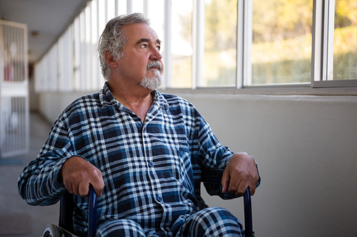 thoughtful senior man looking through window while sitting on . in nursing home