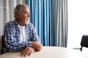 Thoughtful senior man looking away while sitting at table in nursing home