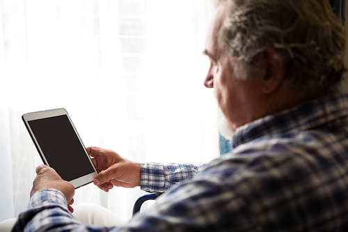 Side view of senior man using digital tablet by window in nursing home