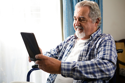 smiling senior man using digital tablet by sitting on . in nursing home