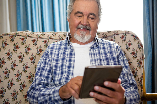 Smiling senior man using digital tablet on sofa in nursing home