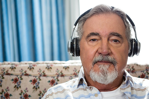 Close up portrait of senior man wearing headphones on sofa in nursing home