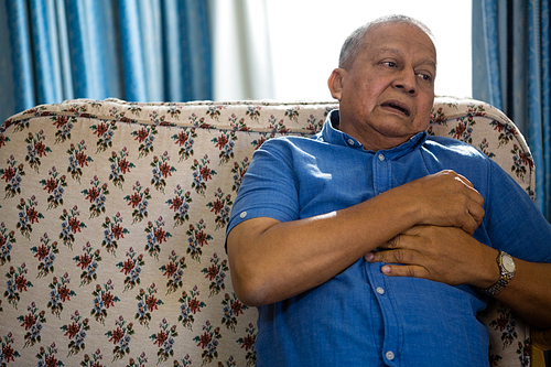 Sad thoughtful senior man looking away while sitting on sofa in nursing home