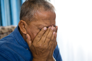 Close up of upset senior man covering eyes with hands in nursing home